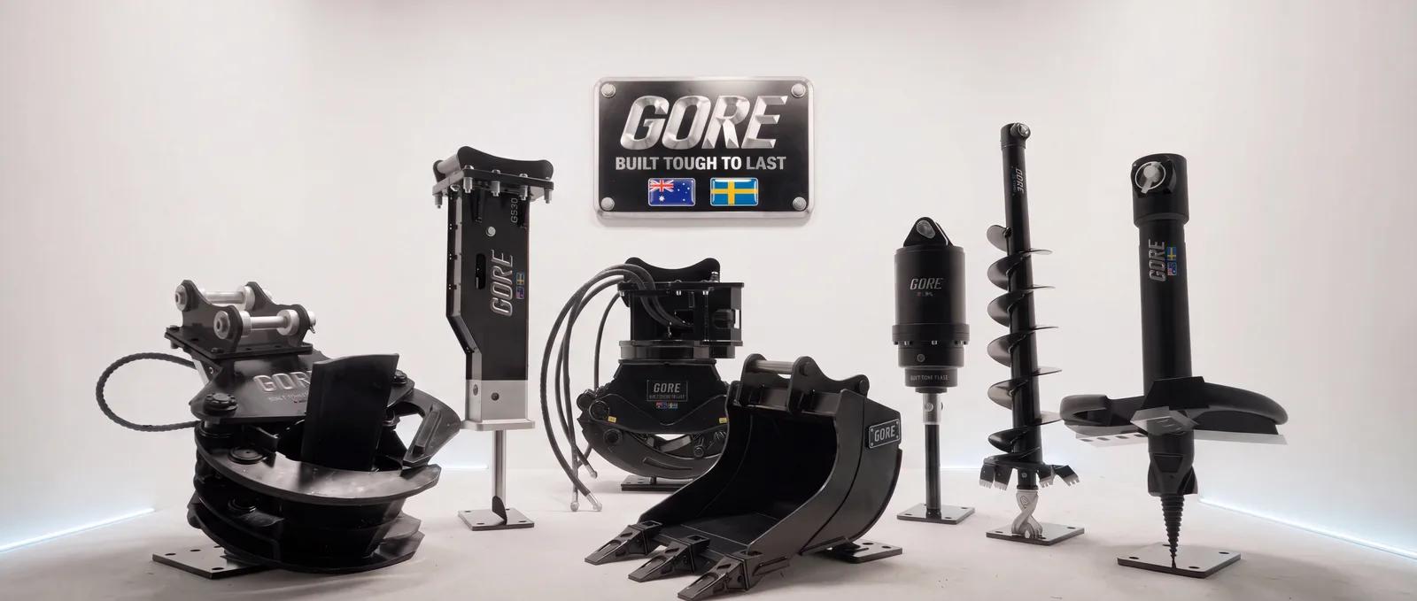 GORE attachments on display under the GORE sign: rotating grapple, hammer, grapple, bucket, auger drive, auger and stump planer