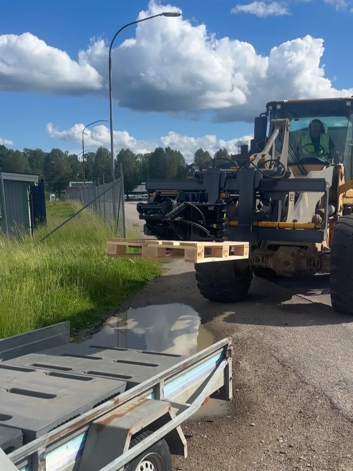 Wheel loader with pallet forks loading a pallet of attachments onto a trailer
